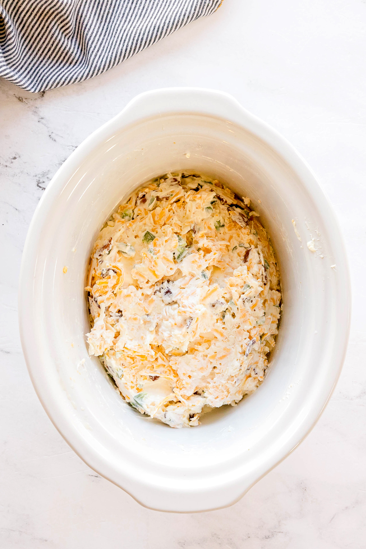 A slow cooker filled with a mixture of cream cheese, sour cream, mayonnaise, sharp cheddar cheese, Monterey Jack cheese, garlic powder, onion powder, Fresh jalapeños, bacon and green onions, ready to be cooked. This is one of the step in preparing Crockpot Jalapeno Popper Dip