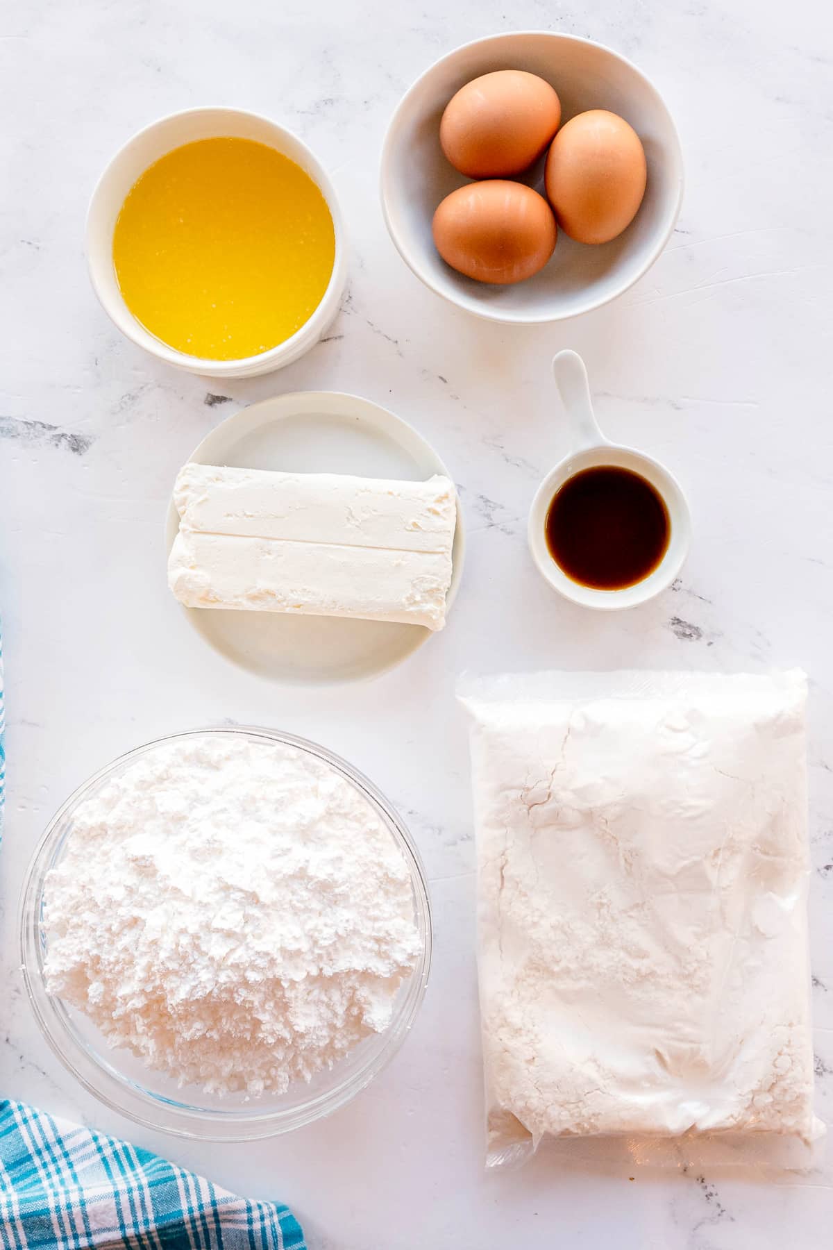 A flat lay of Gooey Cake ingredients including eggs, melted butter, cream cheese, vanilla extract, confectioners sugar, and yellow cake mix on a white surface.