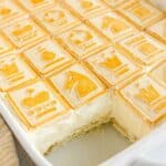 A baking dish filled with creamy Paula Deen Banana Pudding is topped with square cookies featuring chess-themed designs; a serving is missing from one corner.