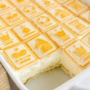 A baking dish filled with creamy Paula Deen Banana Pudding is topped with square cookies featuring chess-themed designs; a serving is missing from one corner.