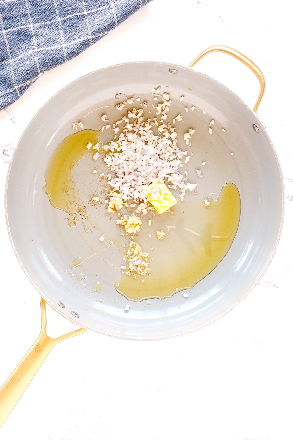 Frist step in preparing Pasta Alla Vodka is to use a white skillet and add olive oil, butter, garlic, and shallots.