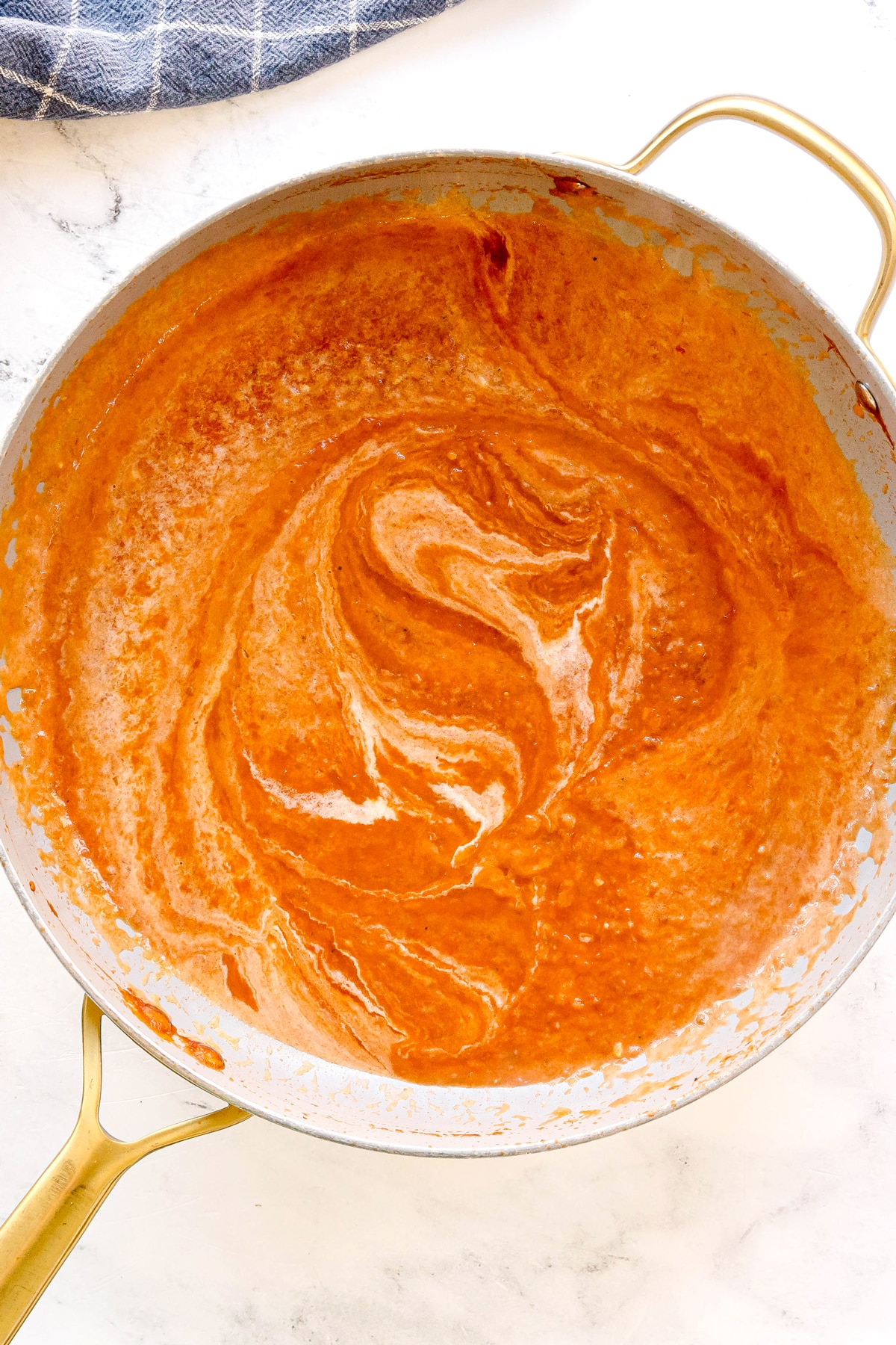 A skillet of tomatoe sauce added with heavy cream is being stirred for Pasta Alla Vodka recipe, showing a swirl pattern on the surface.