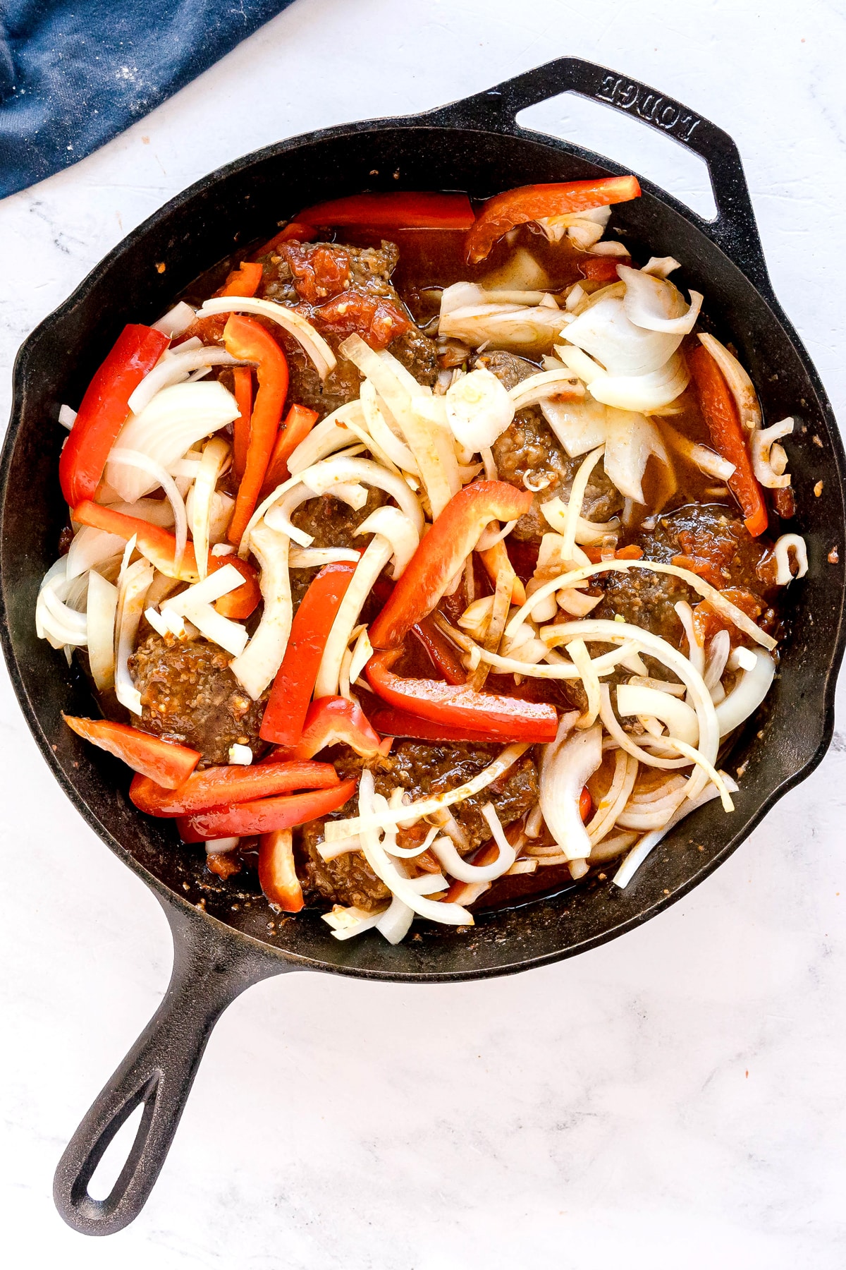 Next step in preparing Swiss Steak is to add water, sliced onion, and bell pepper on a cast iron skillet.
