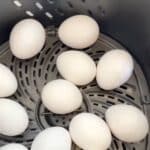 A dozen white eggs arranged in a single layer inside an air fryer basket.