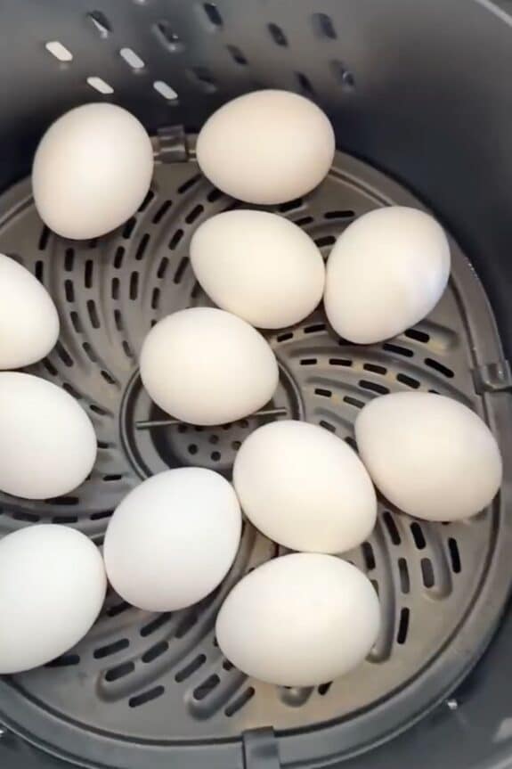 Twelve white eggs are arranged inside the basket of an air fryer.