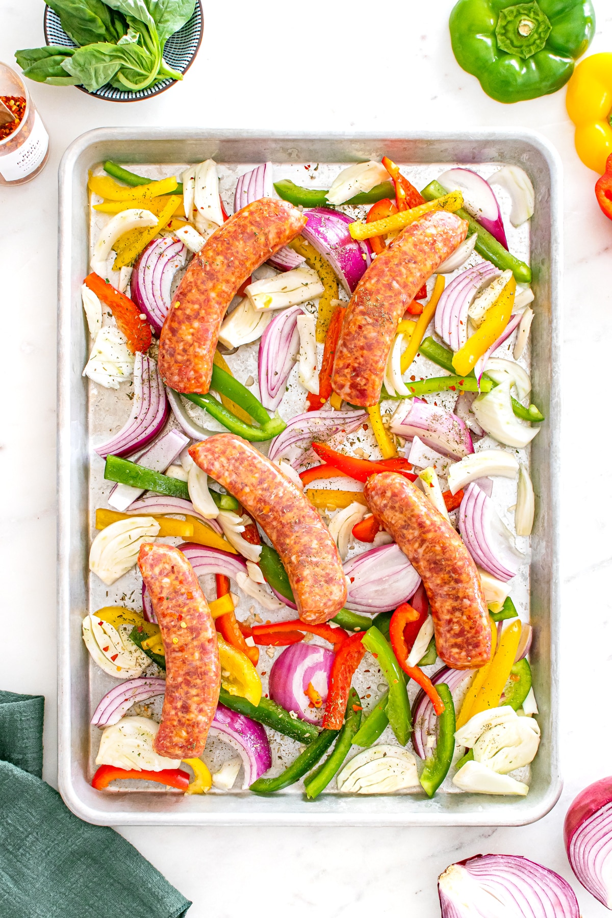 First step in preparing Sheet Pan Sausage and Pepper is to arrange your bell peppers, onions, fennel, and garlic on a large rimmed sheet pan. Drizzle with olive oil and season with salt, pepper, and Italian seasoning. Toss to combine and then arrange in a single layer. 