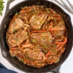 A cast iron skillet filled with cooked steak pieces, bell peppers, onions, and tomato-based sauce—this delicious Recipe For Swiss Steak is garnished with chopped parsley.