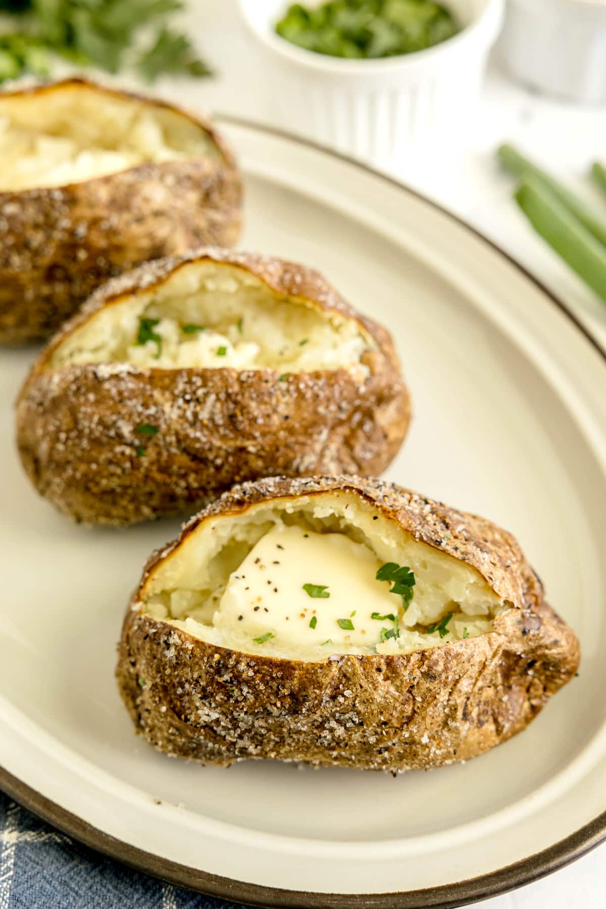 Three baked potatoes with butter and chopped herbs are served on a white plate.