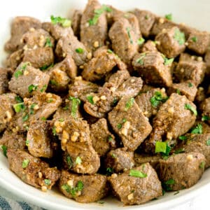 A bowl filled with bite-sized pieces of cooked Air Fryer Steak Bites, garnished with chopped parsley and minced garlic.