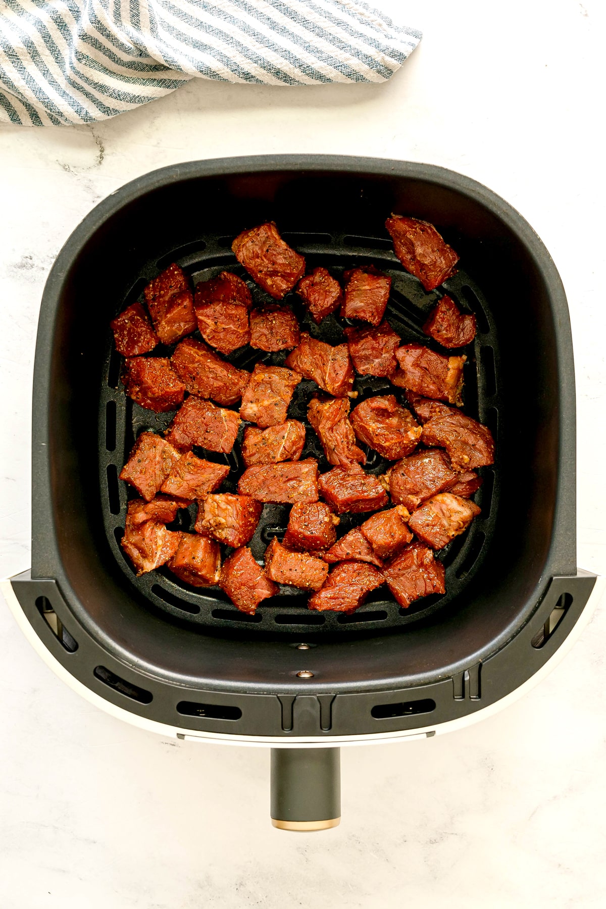 Next process in preparing Air Fryer Steak Bites is to add chunks of seasoned beef in a single layer inside an air fryer basket, ready to be cooked.