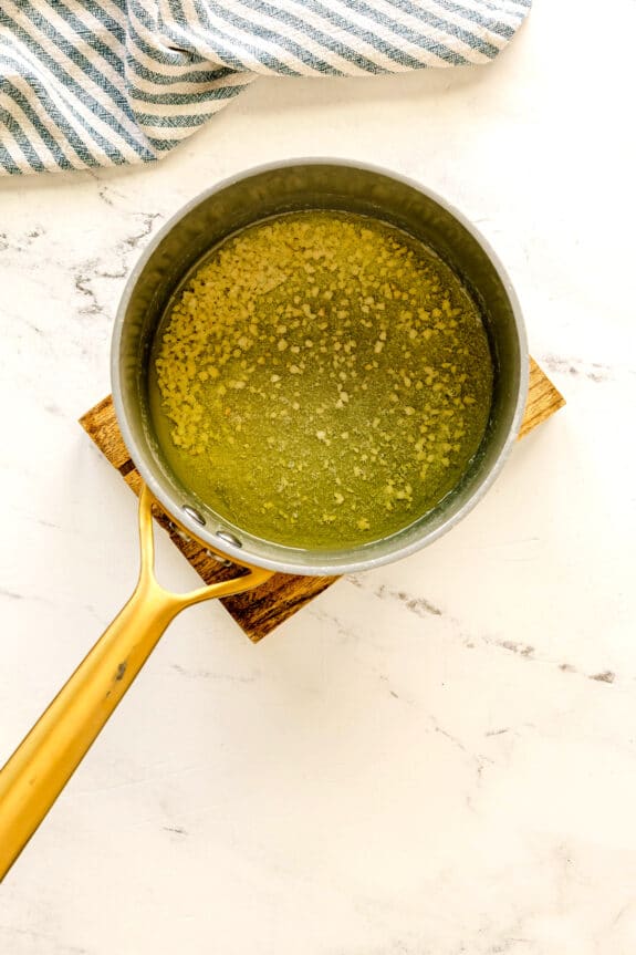 While waiting for the steak to cook, melt butter, and miched garlic for Air Fryer Steak Bites recipe, a wooden trivet on a marble countertop with a striped towel nearby, can also be seen.