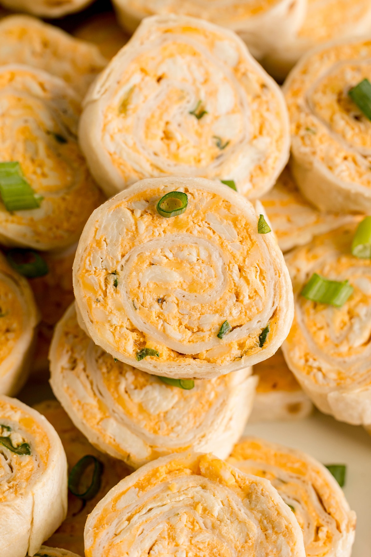 Close-up of Buffalo Chicken Pinwheels filled with a creamy orange cheese mixture and garnished with chopped green onions.