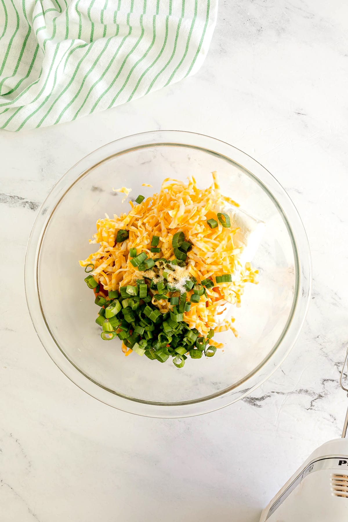 Frist step in preparing Buffalo Chicken Pinwheels is to use a glass bowl. Add the softened cream cheese, ranch dressing, buffalo sauce, shredded cheese, green onions, garlic powder, and salt.