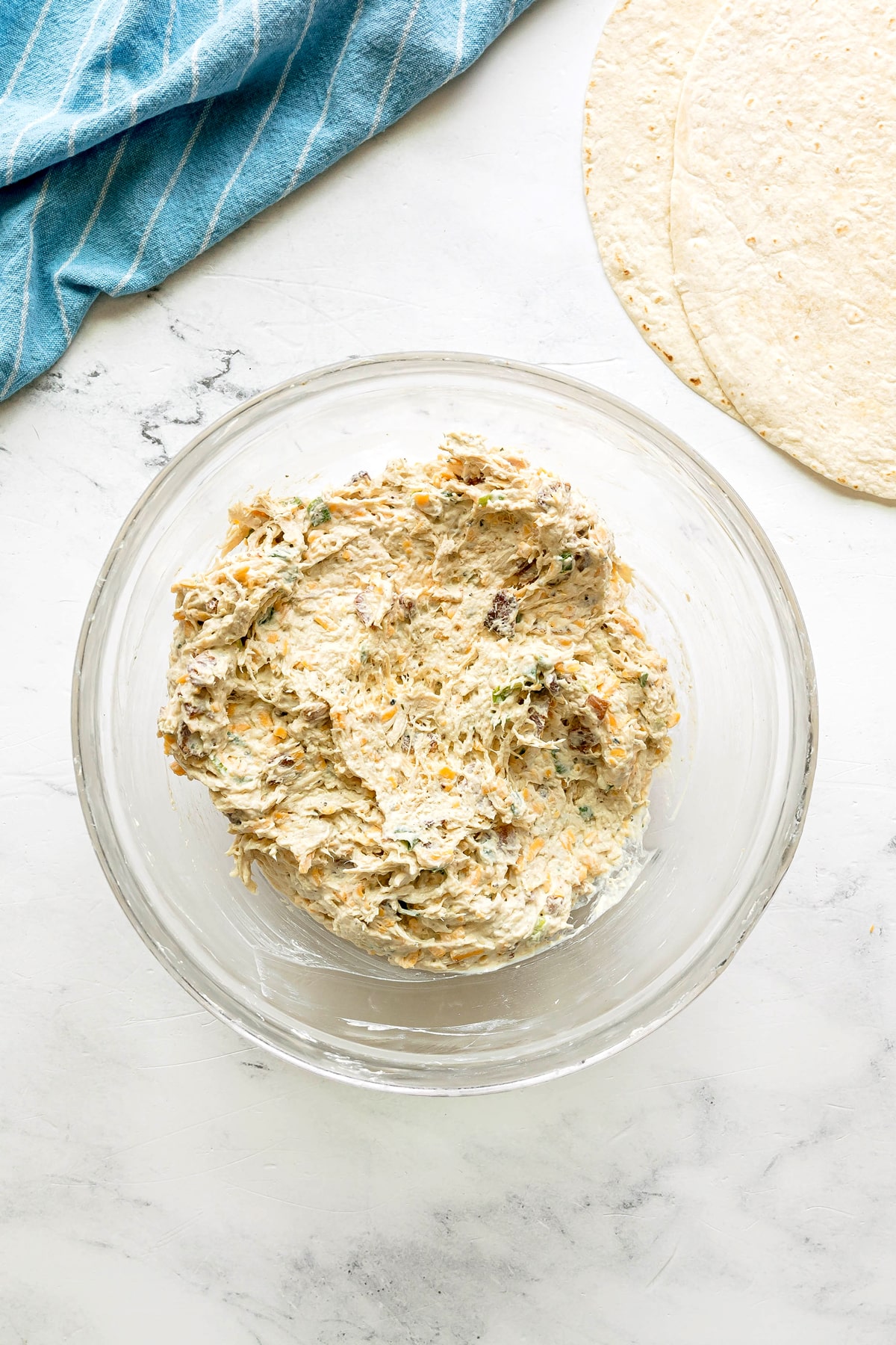 Next step in preparing Easy Crack Chicken Pinwheels is to use a glass bowl and add shredded chicken. Mix until evenly combined.