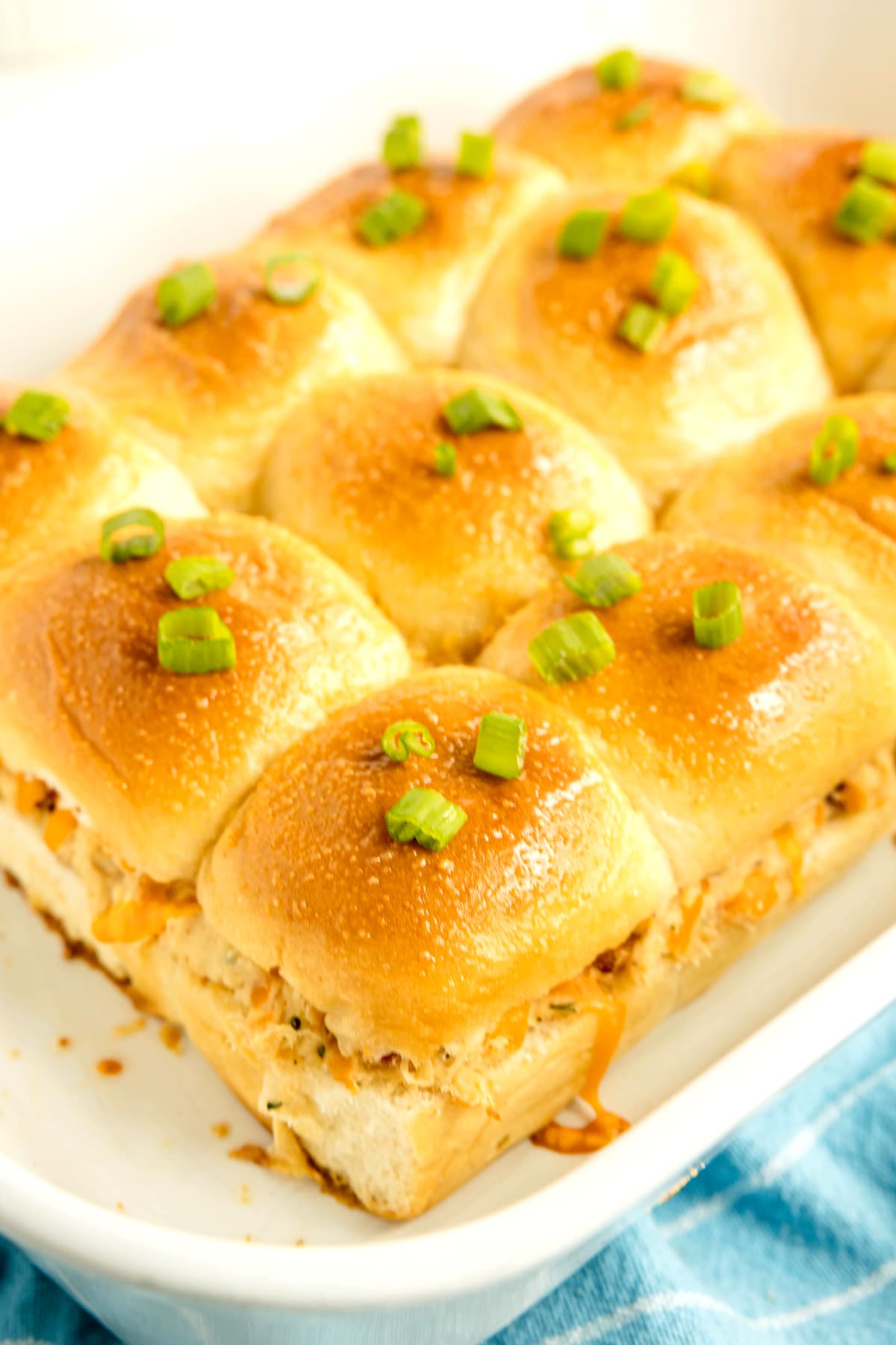 A tray of golden-baked Crack Chicken Sliders filled with shredded meat and topped with chopped green onions.