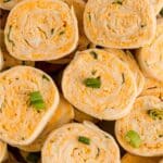 Close-up of several buffalo chicken pinwheels filled with a creamy cheese mixture and garnished with chopped green onions.
