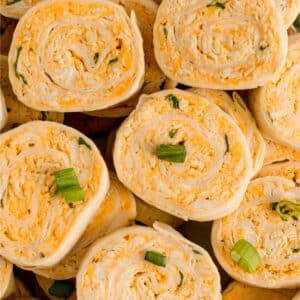 Close-up of several buffalo chicken pinwheels filled with a creamy cheese mixture and garnished with chopped green onions.