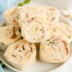 A plate of crack chicken pinwheels features rolled tortillas filled with a savory blend of cream cheese, bacon, shredded cheese, and chopped green onions.