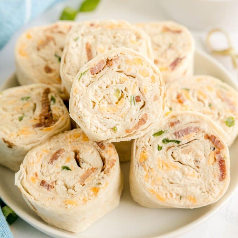 A plate of crack chicken pinwheels features rolled tortillas filled with a savory blend of cream cheese, bacon, shredded cheese, and chopped green onions.
