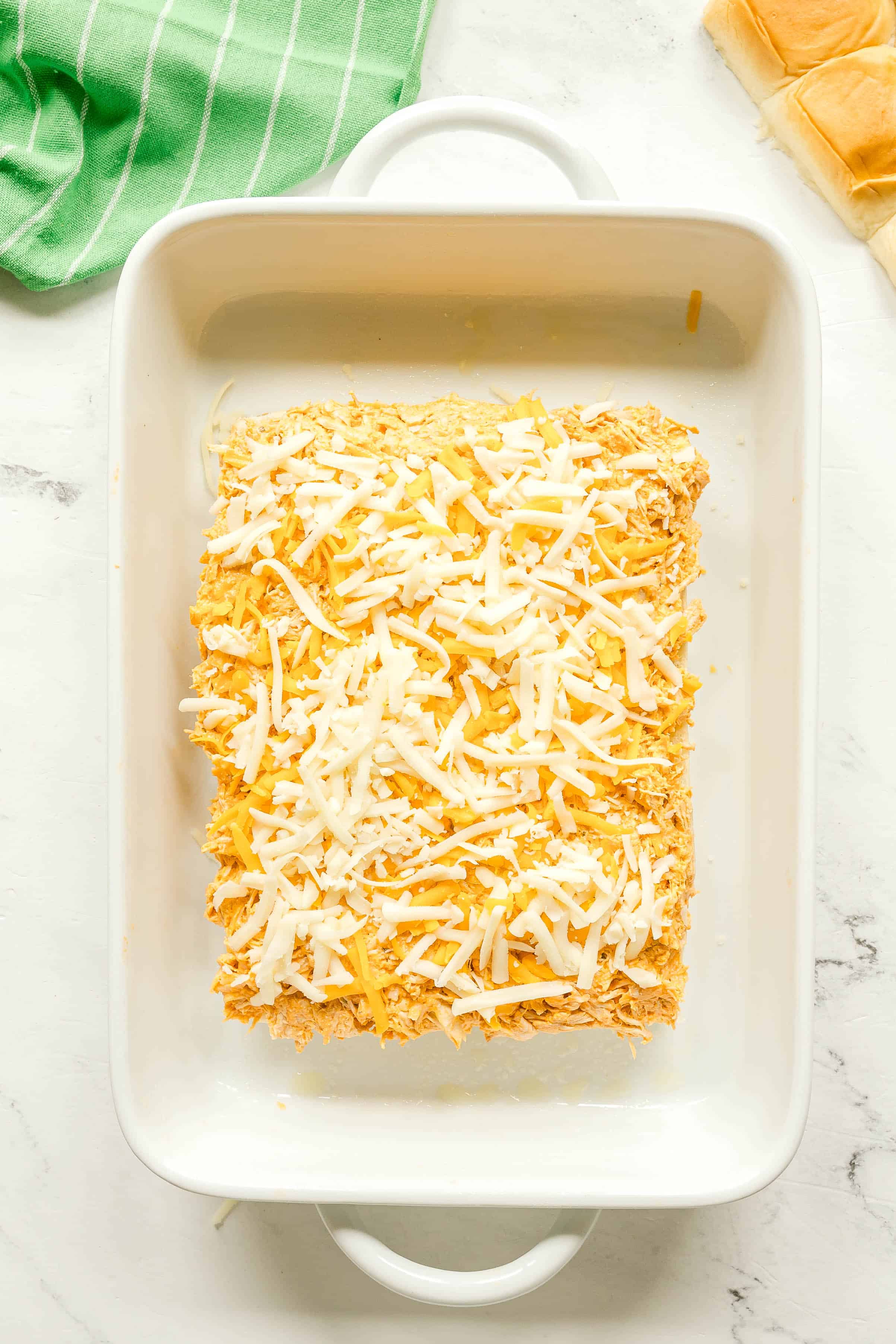Next step in preparing Buffalo Chicken Sliders is to add buffalo chicken mixture evenly over the rolls, cream cheese is also added on top of it.