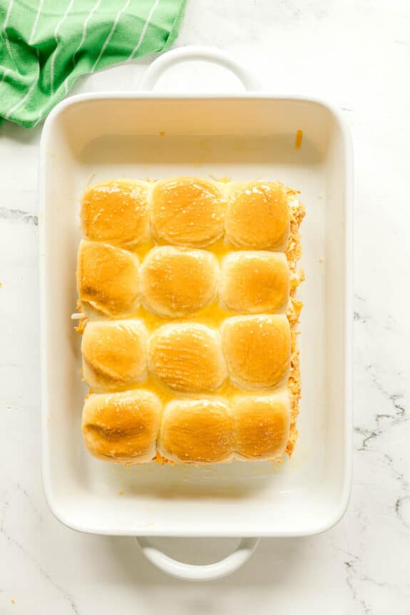 Adding the top portion of Hawaiian rolls and brushing it before baking. This is another step in preparing Buffalo Chicken Sliders