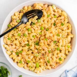 Bowl of macaroni Hawaiian salad with creamy dressing, shredded carrots, and chopped green onions, served with a black serving spoon.