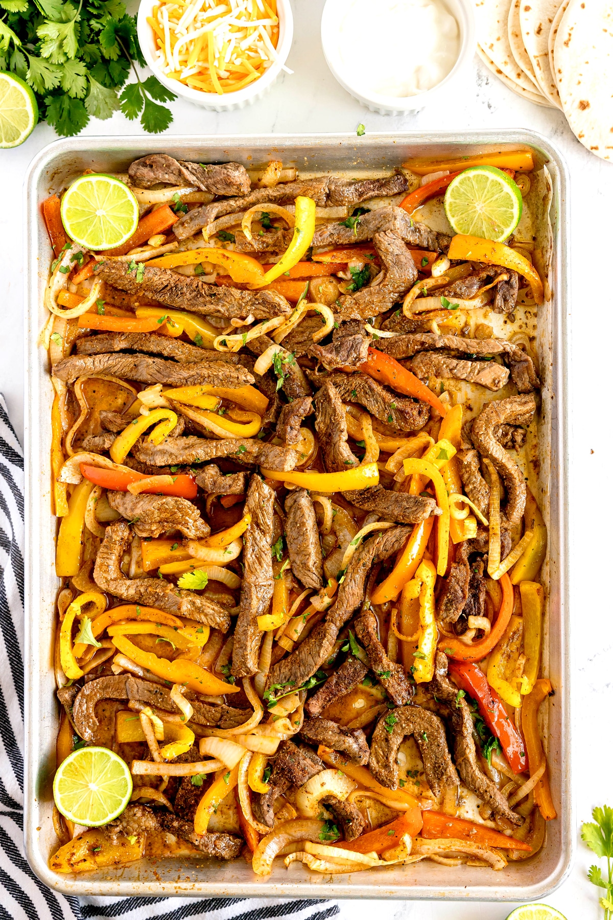 A shSheet Pan Steak Fajitas with sliced bell peppers, onions, and lime wedges.
