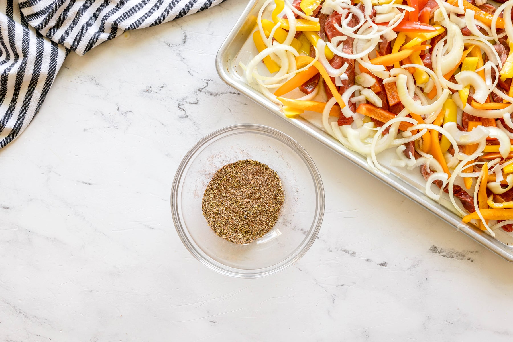 Next step in preparing Sheet Pan Steak Fajitas is to combine the onion powder, garlic powder, cumin, chili powder, chipotle powder, oregano, salt, and black pepper in a small bowl.