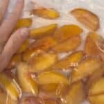 A hand presses on a plastic bag filled with sliced peaches.