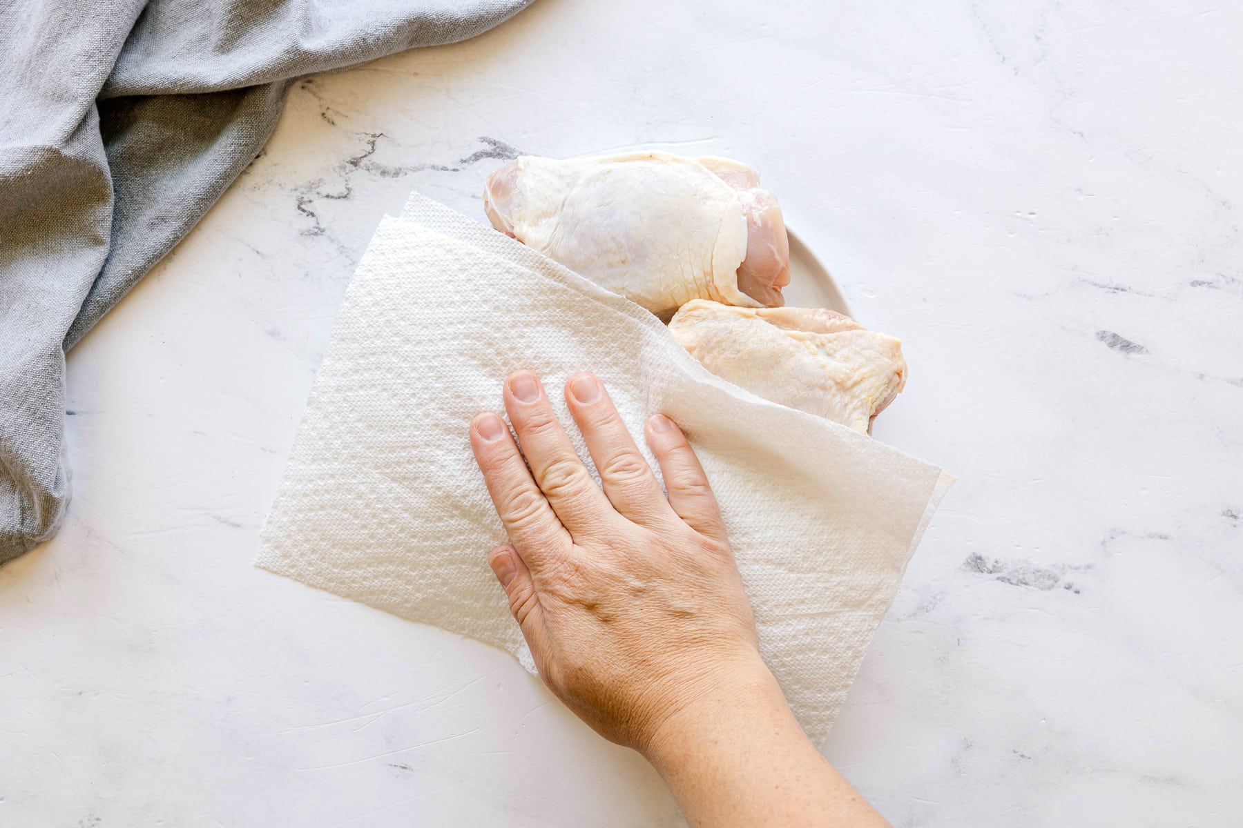 First step in preparing Air Fryer Chicken Thighs is to use a paper towel onto raw chicken pieces on a marble surface, drying them.
