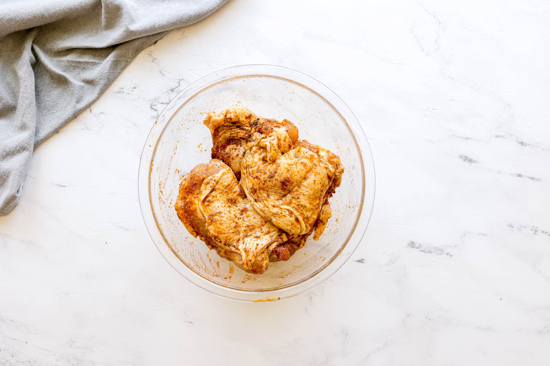 Next step in preparing Air Fryer Chicken Thighs is to marinade the chicken using the spices, gray cloth can also be seen in the photo.