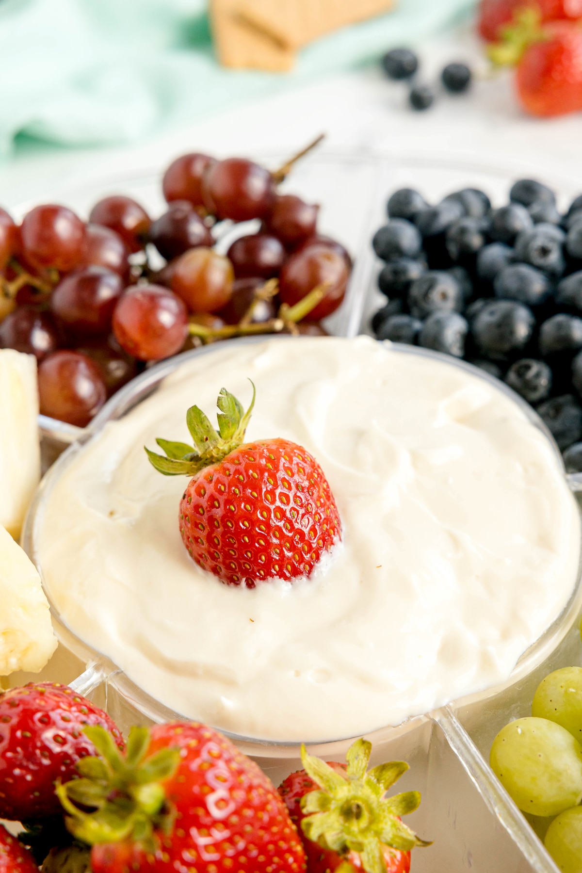 A bowl of Easy Fruit Dip topped with a whole strawberry, surrounded by strawberries, grapes, blueberries, and pineapple pieces.