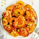 A plate of Huli Huli Chicken garnished with pineapple rings and chopped green onions, served on a white dish.