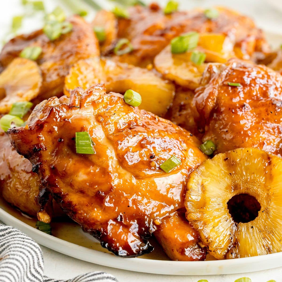 Glazed chicken thighs with pineapple slices and chopped green onions are served on a white plate, inspired by a classic Recipe For Huli Huli Chicken.