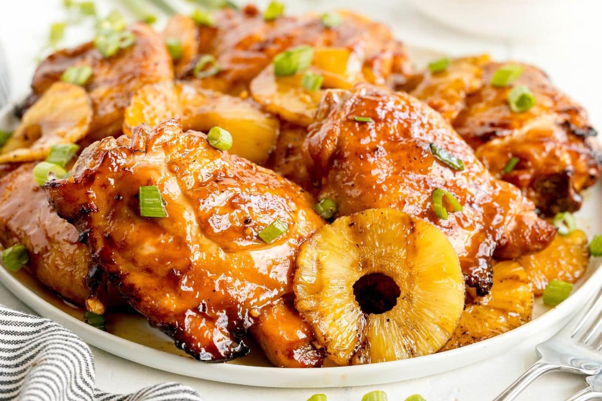 Plate of glazed chicken thighs garnished with chopped green onions and pineapple slices, inspired by a classic Recipe For Huli Huli Chicken, served beautifully on a white plate.