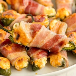 A plate of jalapeno poppers wrapped with bacon, stuffed with creamy cheese and cooked until crispy perfection.