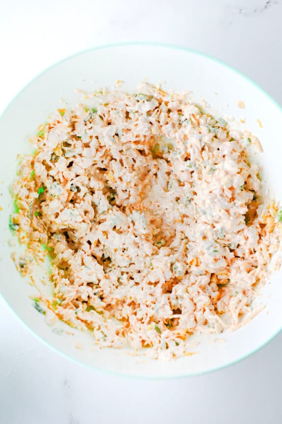 A white bowl containing a mixture of corn, cheddar cheese, diced jalapenos, chili powder, garlic powder, salt, pepper and smoked paprika for Jalapeno Corn Dip recipe.