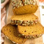 A loaf of pumpkin bread, inspired by the Starbucks Pumpkin Bread Recipe, topped with pumpkin seeds and partially sliced on a wooden cutting board.