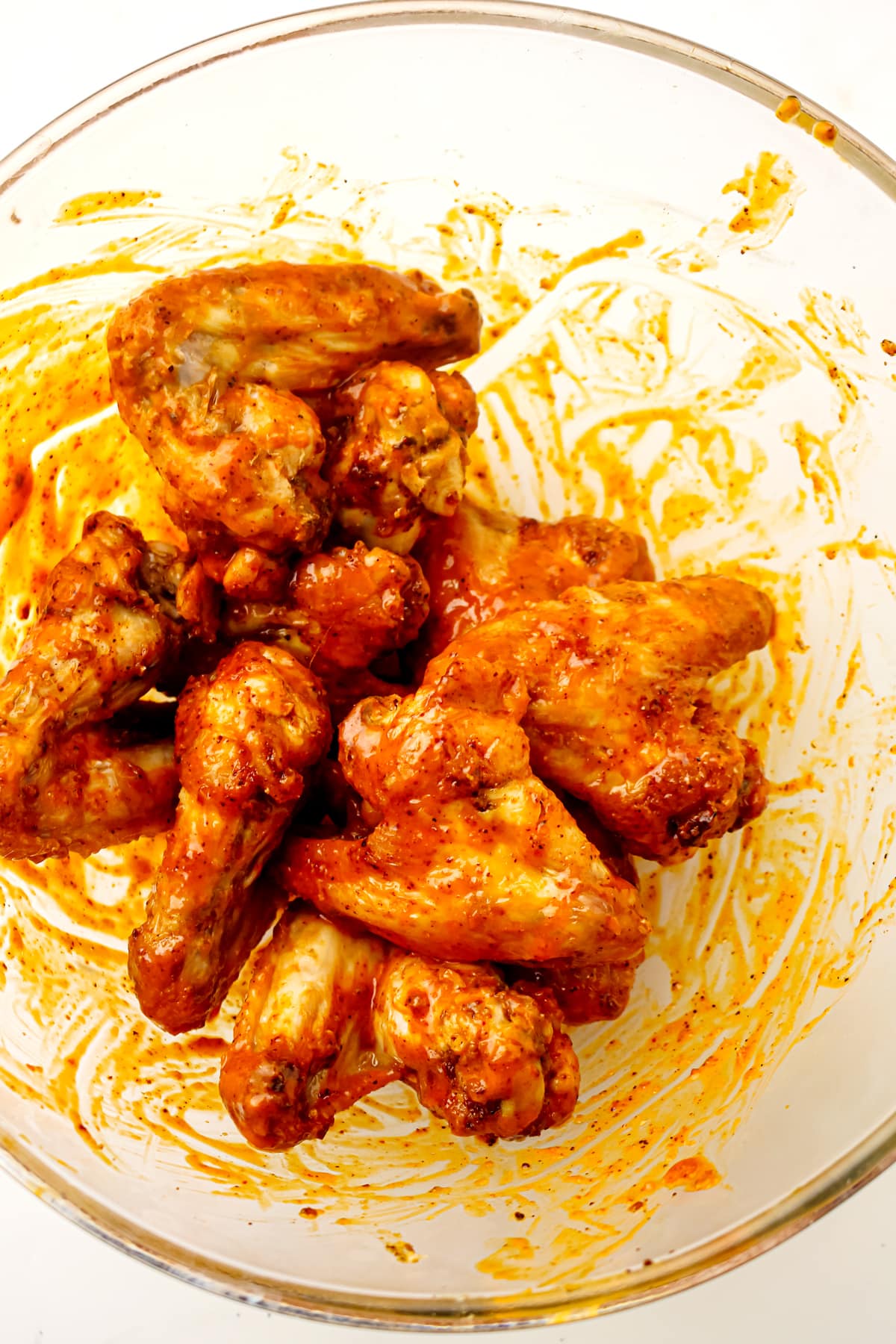 Halfway done Air Fryer Frozen Chicken Wings Chicken wings coated in buffalo sauce are piled in a clear glass mixing bowl.