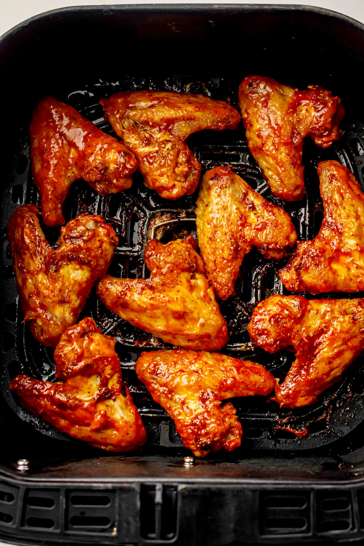 Freshly cooked, Air Fryer Frozen Chicken Wings coated in sauce arranged in a single layer inside an air fryer basket.