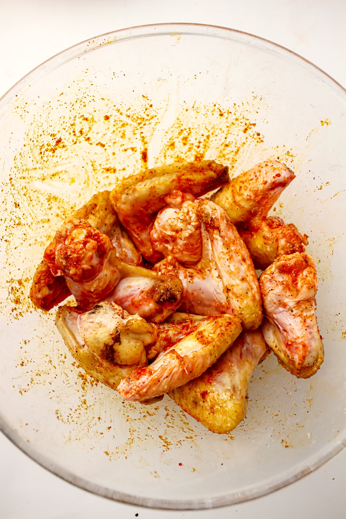 Raw chicken wings coated with seasoning and spices in a clear glass bowl for Air Fryer Frozen Chicken Wings recipe, ready to be cooked.