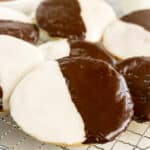 A close-up of Black and White Cookies on a cooling rack, each frosted with half white and half chocolate icing.