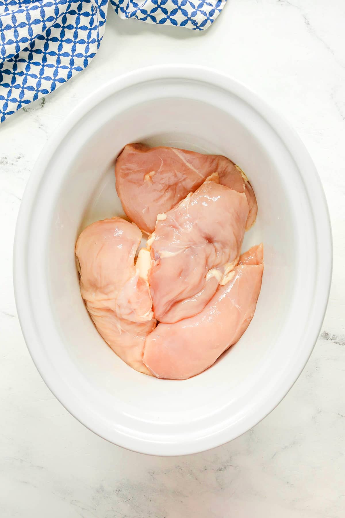 First step in preparing Slow Cooker Chicken and Noodles is to add raw skinless chicken breasts and butter in a slow cooker.
