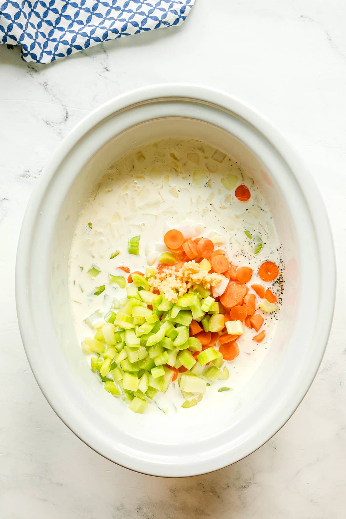 Next step in preparing Slow Cooker Chicken and Noodles is to add cream of chicken soup, chicken stock, heavy cream, black pepper, onion, carrots, celery, and garlic in a slow cooker.