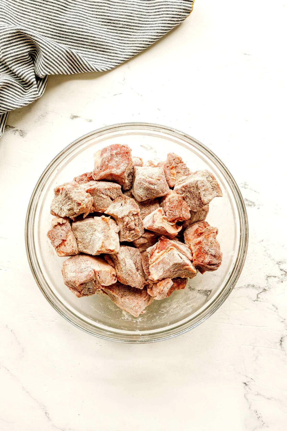 First step in preparing Crockpot Guinness Beef Stew is to use a glass bowl and fill it up with salt, flour, pepper and paprika, resulting to raw, flour-dusted beef chunks.