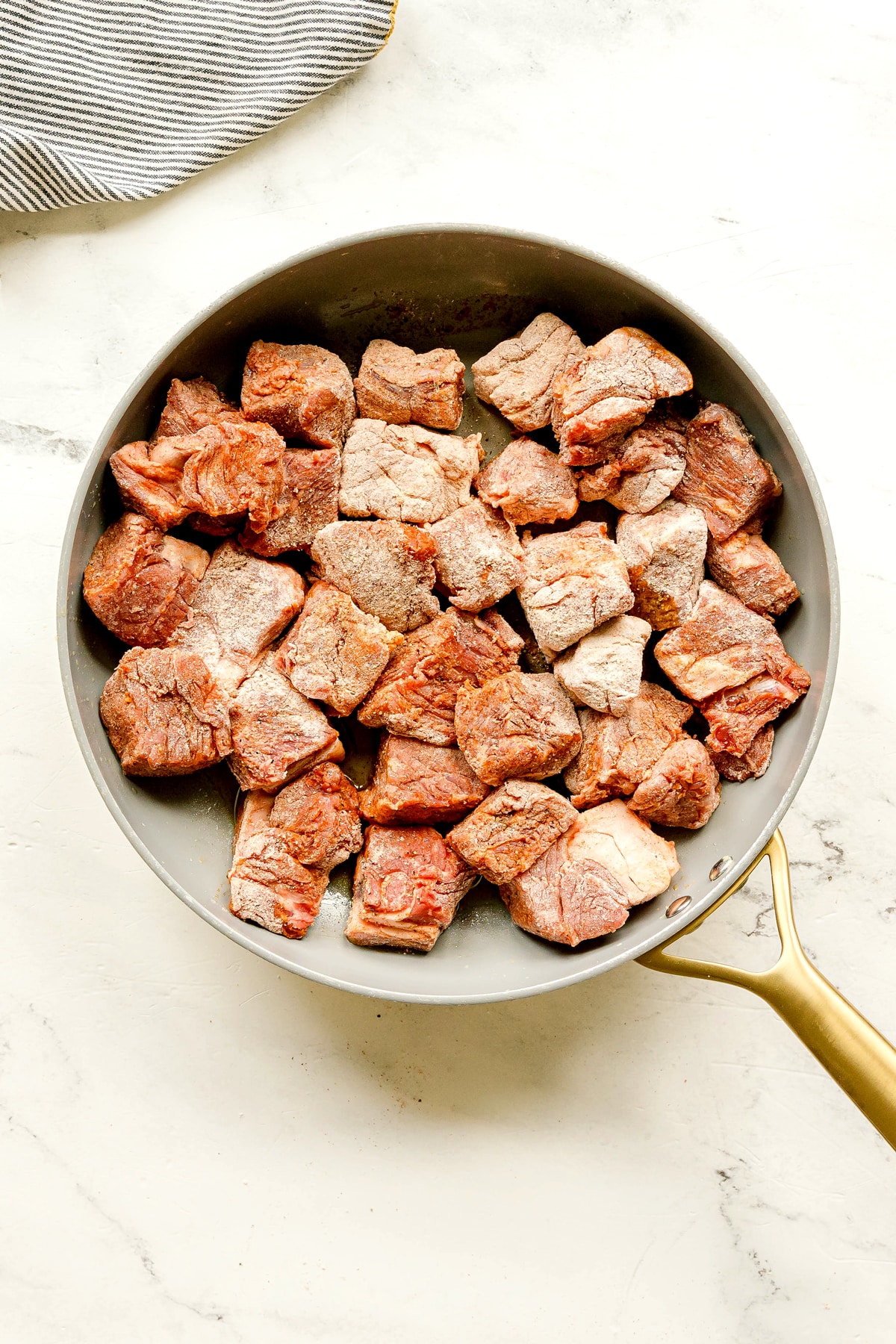 Next step in preparing Crockpot Guinness Beef Stew is to heat oil in a pan and add chunks of raw beef coated with seasoning in a skillet. Sear the beef in batches