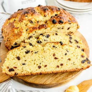 Loaf of raisin-studded Irish soda bread on a wooden cutting board, with a few slices cut, showing its crumbly texture.