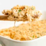 A wooden spoon holds a serving of cheesy Ritz Cracker Casserole above a white baking dish filled with the same casserole.