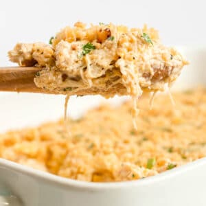 A wooden spoon holds a serving of cheesy Ritz Cracker Casserole above a white baking dish filled with the same casserole.