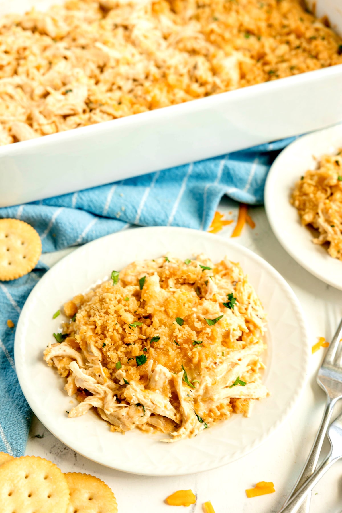 A serving of Ritz Cracker Casserole topped with crushed crackers on a white plate, next to a casserole dish and round crackers.